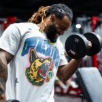 A determined man with tattoos lifting dumbbells in a gym setting.