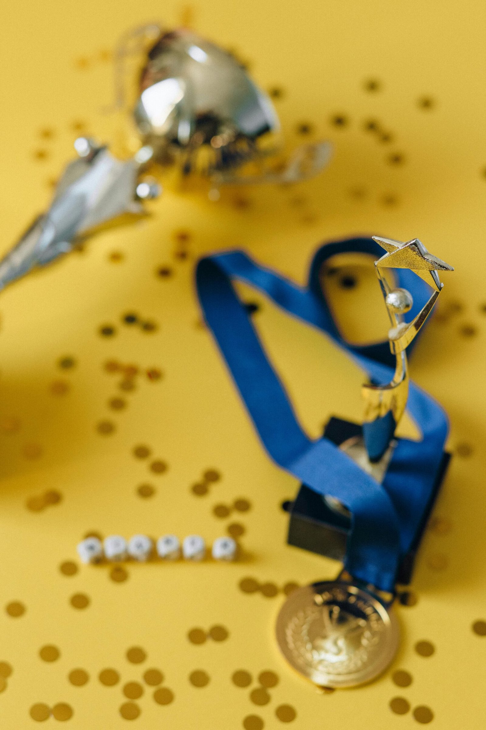 Close-up of a trophy and medal with confetti on a yellow background, symbolizing achievement.